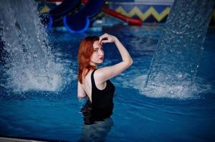 fille sexy aux cheveux rouges en maillot de bain noir se reposant dans la piscine du parc aquatique. photo