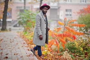 élégant modèle d'homme afro-américain en manteau gris, cravate de veste et chapeau rouge contre les feuilles jaunes humeur d'automne. photo