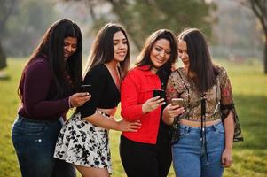 groupe de quatre filles latinos heureuses et jolies de l'équateur posées dans la rue et regardant les téléphones portables. photo