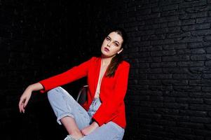 fille brune élégante sur une veste rouge contre le mur de briques noires du studio. photo