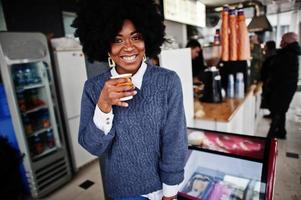 cheveux bouclés femme afro-américaine porter sur pull posé au café intérieur avec une tasse de thé ou de café. photo