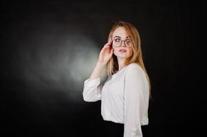 portrait en studio d'une femme d'affaires blonde à lunettes, chemisier blanc et jupe noire sur fond sombre. femme réussie et concept de fille élégante. photo