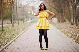 femme afro-américaine élégante en robe jaune posée contre le parc d'automne. photo