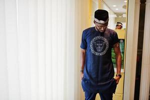 homme africain riche en vêtements traditionnels élégants et chapeau à lunettes posé dans la chambre. photo