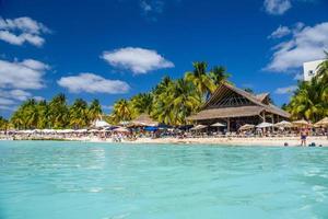 gens prenant un bain de soleil sur la plage de sable blanc avec parasols, bar de bungalows et cocotiers, mer des caraïbes turquoise, île d'isla mujeres, mer des caraïbes, cancun, yucatan, mexique photo