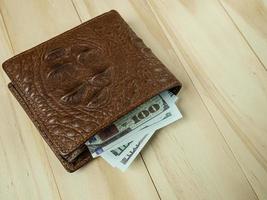 portefeuille en cuir de crocodile et billet de banque sur table en bois. photo