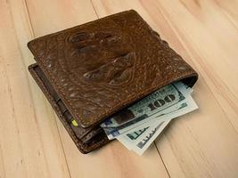 portefeuille en cuir de crocodile et billet de banque sur table en bois. photo