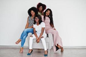 heureux moments positifs lumineux de quatre filles africaines. s'amuser et sourire sur une chaise contre un mur vide blanc. beaux moments de quatre meilleurs amis. photo