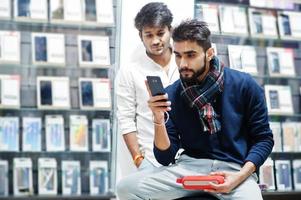 deux indiens mans client acheteur au magasin de téléphonie mobile avec écouteurs et haut-parleur sans fil écoutant de la musique. concept de peuples et de technologies d'asie du sud. magasin de téléphonie mobile. photo