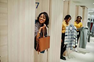 trois femmes africaines choisissant des vêtements au magasin. journée shopping au vestiaire ou cabine d'essayage. photo