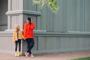 vue horizontale d'une femme européenne à la mode en pull lâche rouge, jeans déchirés, tient la main avec sa sœur cadette, pose dehors ensemble, se promène en plein air, a des relations amicales photo