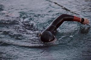 athlète de triathlon nageant sur le lac au lever du soleil portant une combinaison de plongée photo