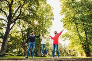 portrait d'une famille amicale et affectueuse s'amuser ensemble, passer du temps libre à l'extérieur, se tenir contre des arbres verts dans le parc, essayer de bercer un petit enfant dans les mains. trois membres de la famille jouent sur la nature photo