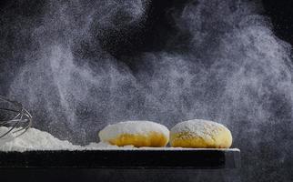 ébauches de pâte crue sur fond noir. notion de boulangerie. la farine se déverse sur la table. photo avec espace de copie.