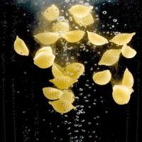 pâtes en forme de coquille tombant dans l'eau sur fond noir. photo