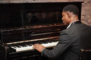 le dos d'un homme afro-américain puissant et puissant en costume noir joue du piano. photo