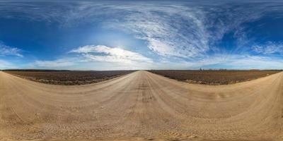 panorama hdri sphérique complet et harmonieux vue à 360 degrés sur la route de gravier parmi les champs au printemps avec des nuages impressionnants en projection équirectangulaire, prêt pour le contenu de réalité virtuelle vr ar photo