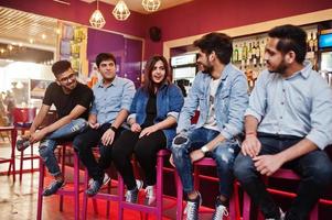 un groupe d'amis asiatiques élégants portent des jeans assis sur des chaises contre un bar dans un club et discutent ensemble. photo