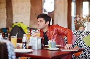 homme indien élégant en tenue décontractée assis café intérieur et boire du jus. photo