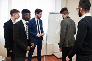 des collègues masculins travaillant en équipe coopèrent, une équipe multiraciale d'employés s'est concentrée sur la planification de projets contre un tableau à feuilles mobiles et sur la discussion d'idées. photo