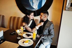 charmant couple indien amoureux, porter au sari et costume élégant, posé sur le restaurant. femme attachée cravate sur son homme. photo