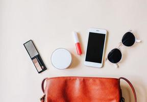 mise à plat d'un sac femme en cuir marron ouvert avec des cosmétiques, des accessoires et un smartphone sur fond jaune avec espace de copie photo