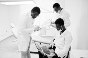 trois médecins afro-américains travaillant avec un ordinateur portable, discutant avec des collègues de la clinique dentaire. photo