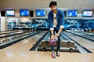 barbe élégante homme asiatique en chemise jeans debout au bowling avec ballon à portée de main. photo