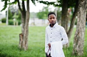 un jeune médecin afro-américain tient un manteau blanc à portée de main avec un stéthoscope posé à l'extérieur. photo