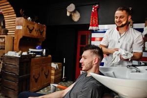 jeune homme barbu se lavant la tête par le coiffeur alors qu'il était assis sur une chaise au salon de coiffure. âme de barbier. photo