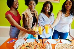 quatre jeunes filles africaines dans une pizzeria aux couleurs vives qui trinquent. photo