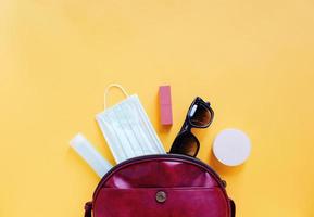 mise à plat d'un sac femme en cuir rouge ouvert avec des cosmétiques, des accessoires et un masque avec désinfectant au gel d'alcool sur fond jaune, espace de copie et prévention du concept covid-19 et coronavirus photo