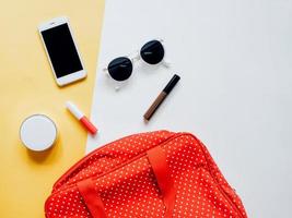 mise à plat du sac femme à pois rouges ouvert avec des cosmétiques, des accessoires et un smartphone sur fond coloré photo