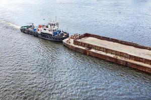 un vieux remorqueur fluvial pousse une barge rouillée vide sur la rivière. photo