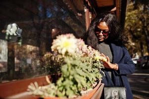 fille afro-américaine élégante en manteau bleu et lunettes de soleil posées à la journée d'automne ensoleillée. femme modèle afrique. photo