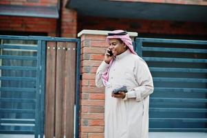 homme d'affaires arabe du moyen-orient posé dans la rue contre un bâtiment moderne avec tablette et téléphone portable à portée de main. photo