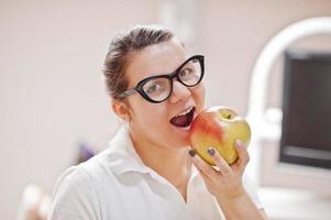 portrait d'une femme dentiste debout dans son cabinet de dentisterie et mangeant une pomme. photo