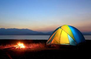 tente et feu de camp au coucher du soleil, au bord du lac photo