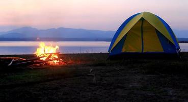 tente et feu de camp au coucher du soleil, au bord du lac photo