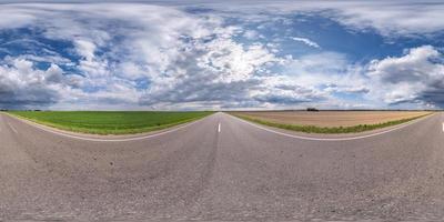 panorama sphérique complet sans couture vue d'angle à 360 degrés sur une route asphaltée sans circulation parmi les champs avec ciel nuageux en projection équirectangulaire, contenu vr ar photo