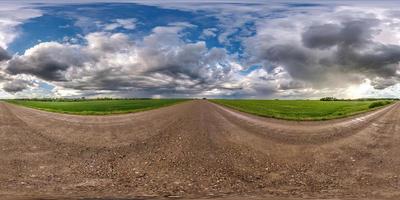 panorama hdri sphérique complet et harmonieux à 360 degrés sur une route de gravier humide parmi les champs au printemps avec des nuages d'orage après la pluie en projection équirectangulaire, prêt pour le contenu vr ar photo