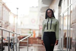 portrait de la ville d'une jeune femme positive à la peau foncée portant un sweat à capuche vert et des lunettes. photo