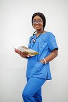 portrait d'une jeune femme médecin afro-américaine heureuse pédiatre en manteau uniforme bleu et stéthoscope avec des livres à mains isolés sur blanc. photo