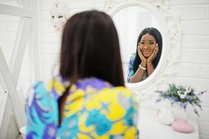 modèle de femme afro-américaine élégance porter des vêtements colorés. femmes afro chics dans la chambre regardant le miroir. photo