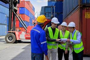 un groupe de travailleurs multiraciaux portant des uniformes de sécurité et des casques durs travaillent au terminal logistique avec de nombreuses piles de conteneurs, chargeant des marchandises d'expédition de contrôle pour l'industrie du transport de fret. photo