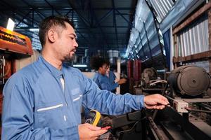 un ingénieur professionnel masculin de l'industrie asiatique en uniformes de sécurité travaille avec des travailleuses en inspectant la tension des machines, en vérifiant et en entretenant à l'usine de fabrication, les professions des services électriques. photo