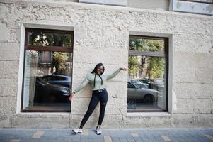 portrait de la ville d'une jeune femme positive à la peau foncée portant un sweat à capuche vert et des lunettes. photo