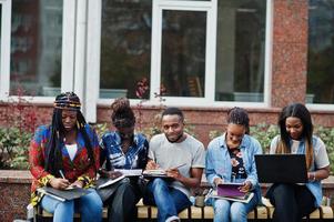 groupe de cinq étudiants africains qui passent du temps ensemble sur le campus de la cour universitaire. amis afro noirs étudiant au banc avec des articles scolaires, des cahiers d'ordinateurs portables. photo