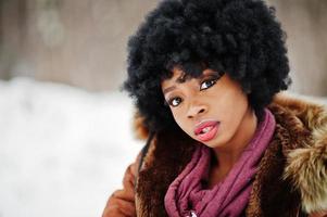 femme afro-américaine aux cheveux bouclés portant un manteau et des gants en peau de mouton posés le jour de l'hiver. photo