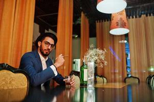 bel homme arabe bien habillé avec un verre de whisky et de cigare posé au pub. photo